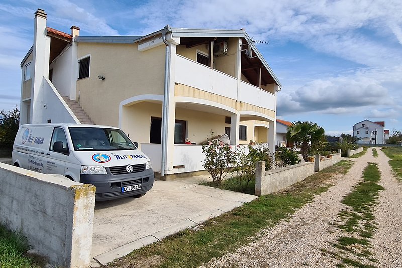 Gemütliches Haus mit Garten, Parkplatz und Autos, umgeben von Natur.