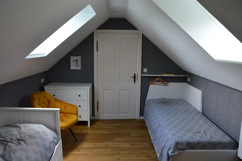 Gezellige slaapkamer met eenpersoonsbedden en fauteuils.