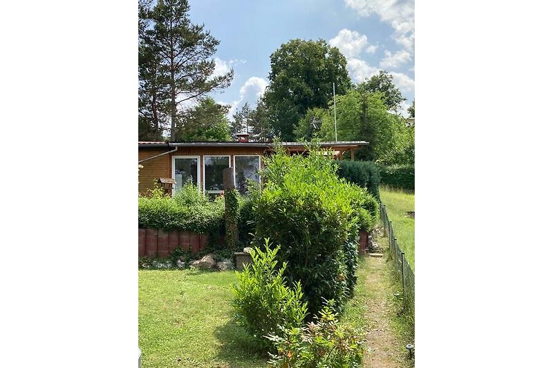 Gemütlicher Garten mit Rasen, Bäumen und einem charmanten Cottage.