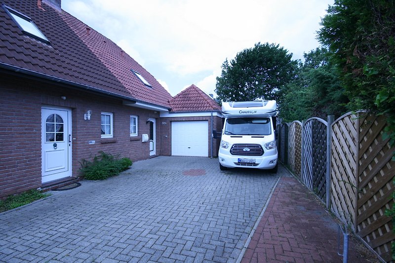 Modernes Haus mit Garage, Garten, Zaun und geparktem Auto.