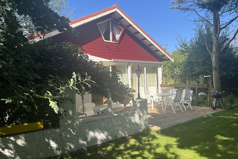 Charmantes Landhaus mit Garten, Veranda und blühenden Sträuchern.