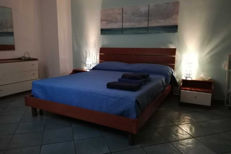 Gemütliches Schlafzimmer mit Holzdekor, Bett, Nachttisch und Lampe.