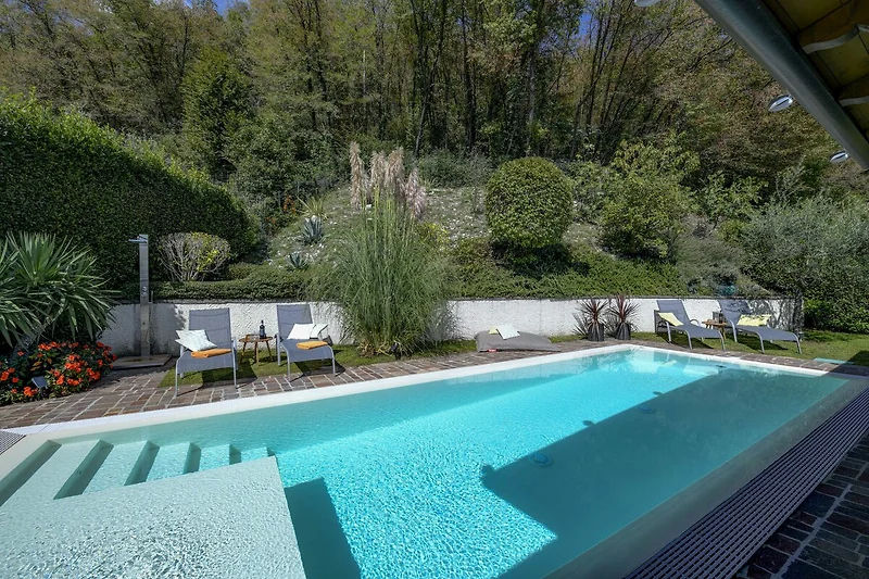 Privater Pool mit Liegestühlen, Sonnenschirm und üppigem Garten.