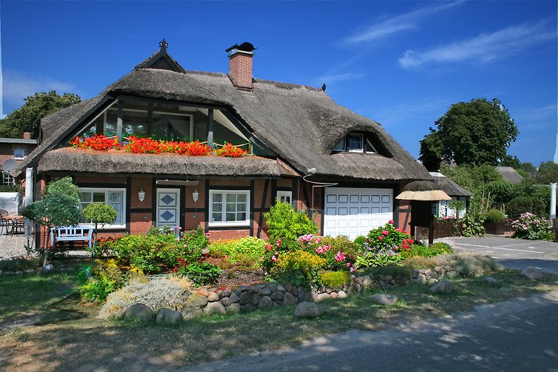 Charmantes Landhaus mit Reetdach, umgeben von üppigem Grün und Bäumen.