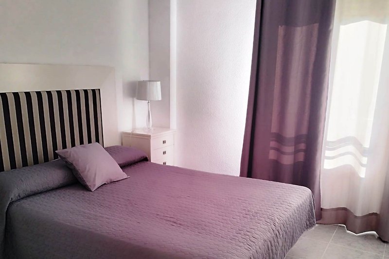 Gemütliches Schlafzimmer mit lila Bettwäsche und Holzmöbeln.