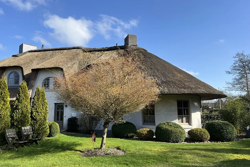 Reetdachhaus mit gepflegtem Garten und grüner Hecke.