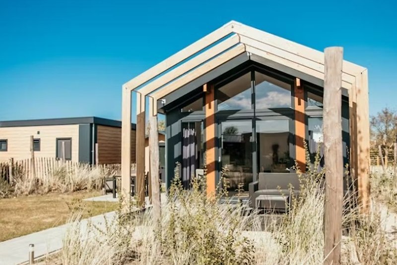 Modern gebouwd chalet, terras met zitbank en chalet-entree via schuifdeuren in een groen landschap.