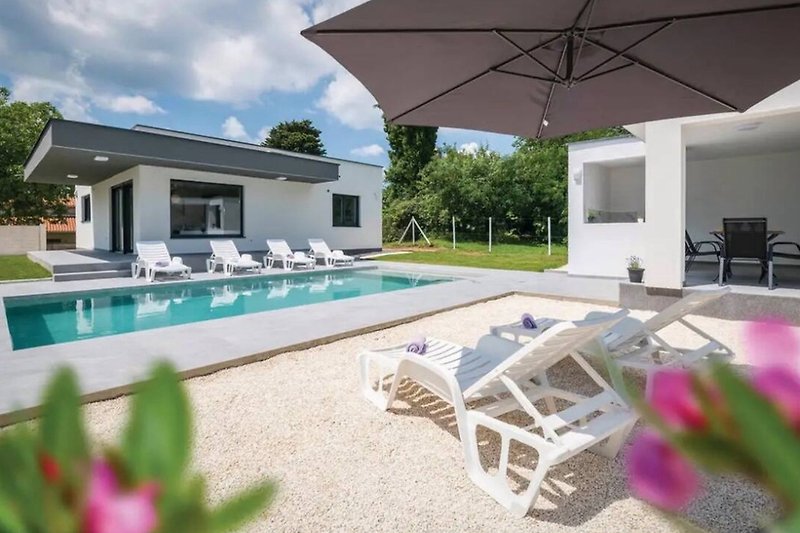 Luxusvilla mit Pool, Sonnenliegen und üppigem Garten.