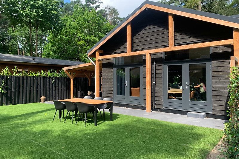 Gemütliches Holzhaus mit Gartenmöbeln und üppiger Landschaft.