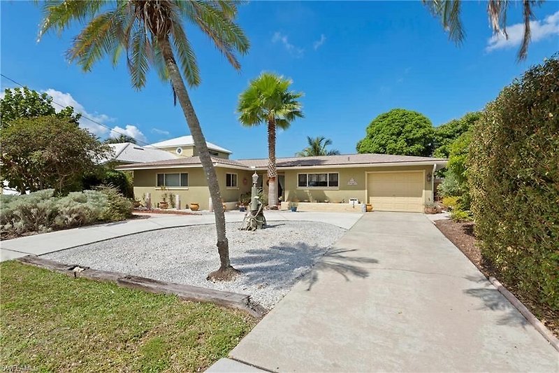 Moderne Villa mit Garten, Palmen und blühender Landschaft.