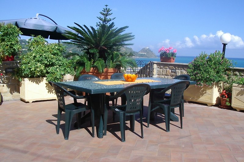 Tropische Terrasse mit Palmen, Tisch und Meerblick.