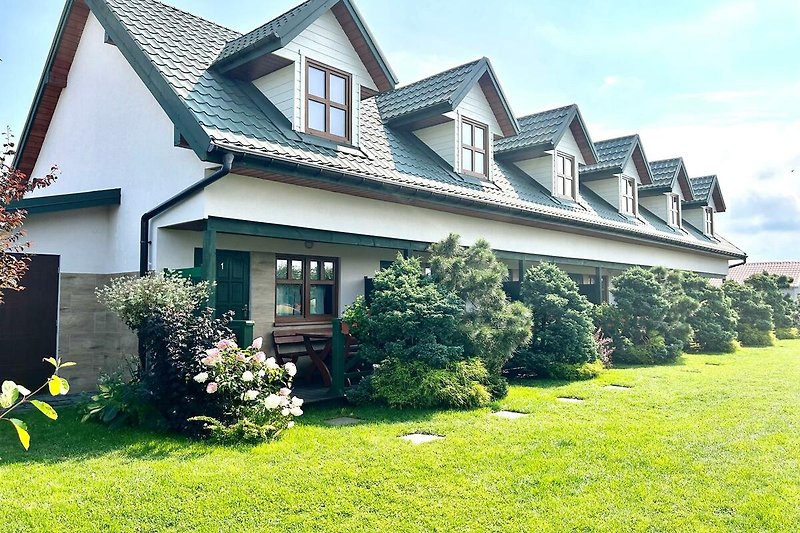 Charmantes Landhaus mit Garten, Bäumen und blühenden Sträuchern.