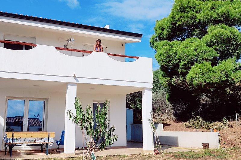 Große Villa mit schattiger Terrasse und weitläufigem Garten.