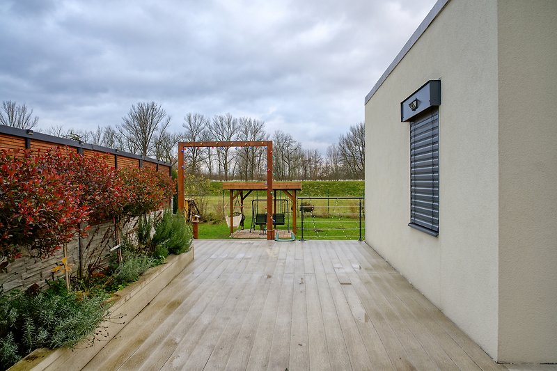 Garten mit Pflanzen, Holzdeck und schattigem Sitzbereich.