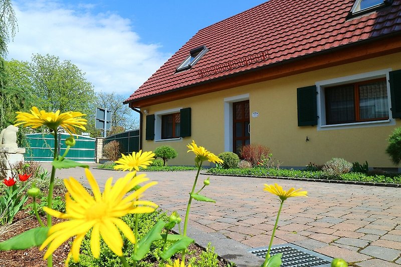 Gelbes Haus mit Garten, Blumen, Gehweg und Einfahrt.