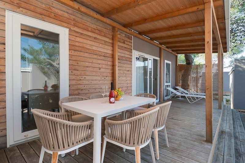 Holzveranda mit Gartenmöbeln und Palmen im Hintergrund.