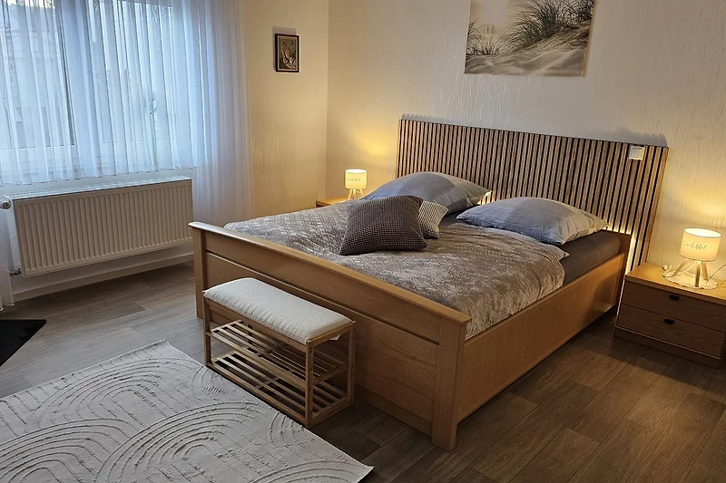 Schlafzimmer mit Holzbettrahmen, Nachttisch und Lampe.
