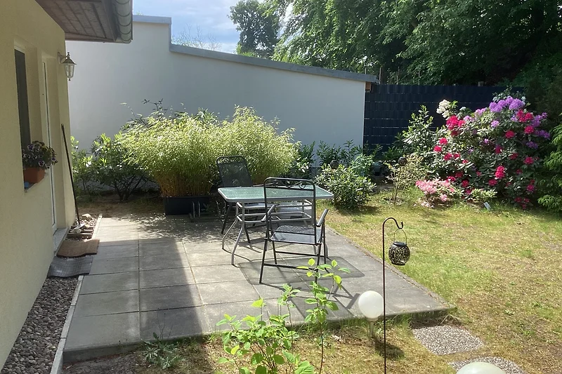 Garten mit Pflanzen, Gartenmöbeln und schattigem Sitzbereich.