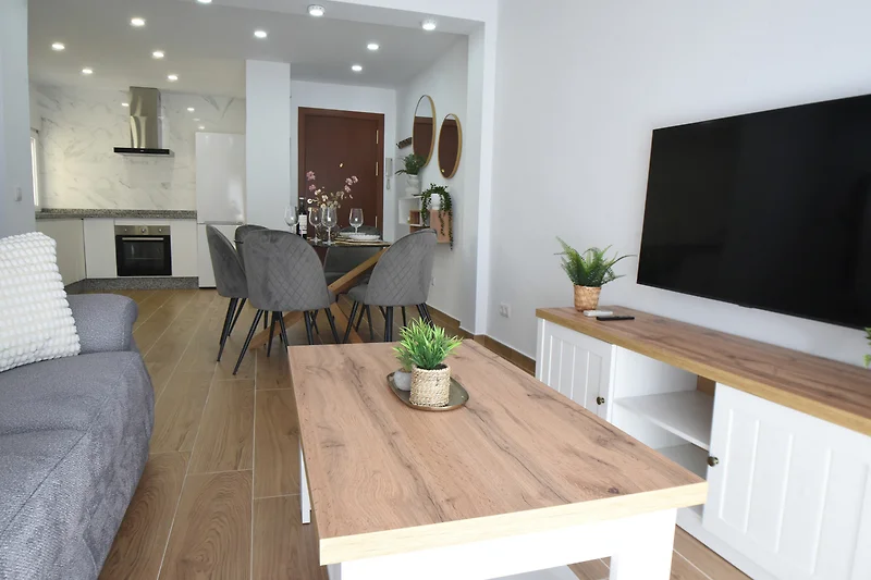 Gemütliches Wohnzimmer mit Holzboden, Couch, TV und Beleuchtung.