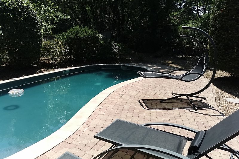 Pool mit Sonnenliegen und schattiger Terrasse im Garten.