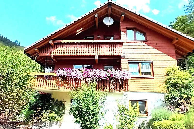 Haus am Wald umgeben von Pflanzen  auf Terrasse und im Garten.