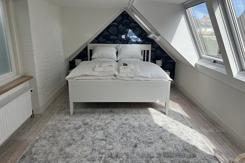 Dachgeschosszimmer mit Bett, Kissen und sanfter Beleuchtung.