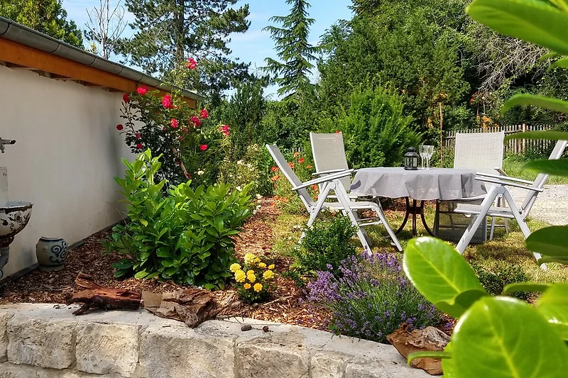 Grüner Garten mit Pflanzen, Steinen und Gartenmöbeln.