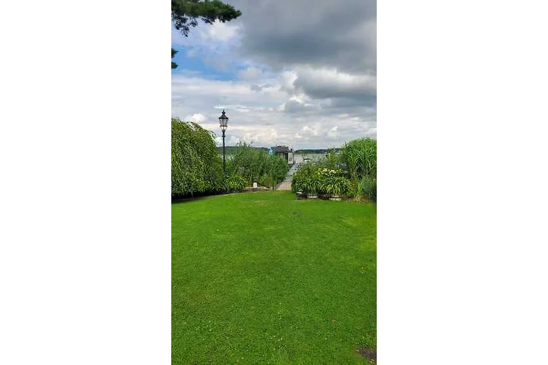 Grüner Garten mit gepflegtem Rasen, Hecken und immergrünen Pflanzen.
Direkter eigener Seezugang mit Steg und Boot.
