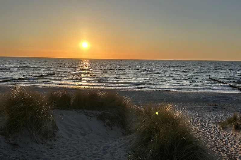Sonnenuntergang am Meer: Wellen, Sand und leuchtender Himmel.