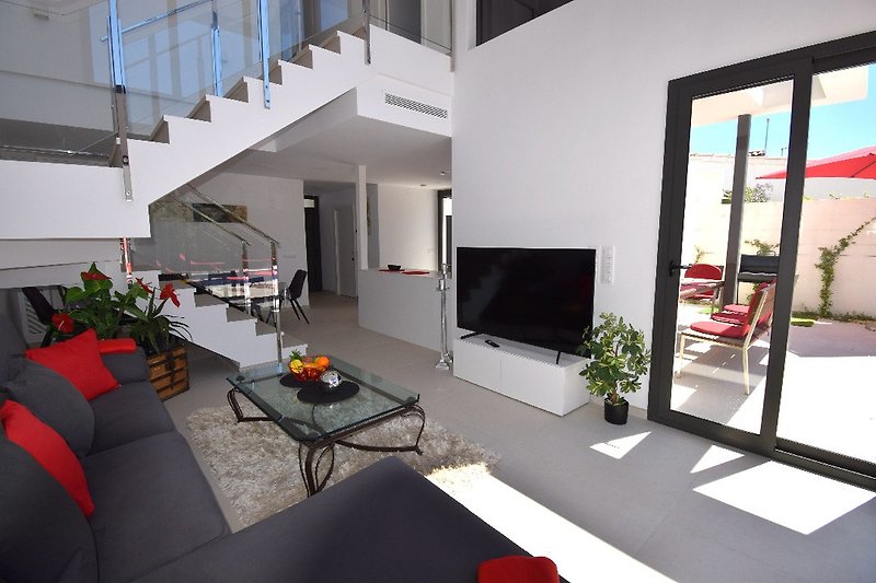 Wohnzimmer mit Couchgarnitur, SAT-TV mit grossem Flachbild-TV, Essbereich mit Tisch und Stühlen für 8 Personen. Treppenaufgang in das OG.