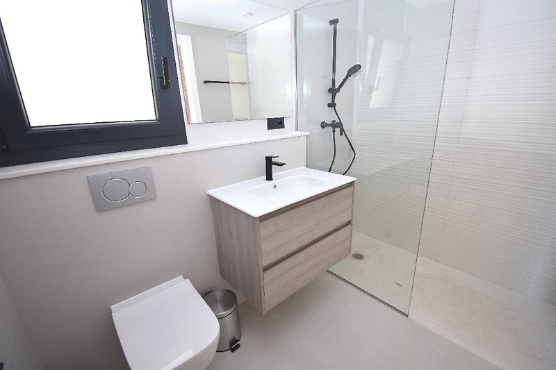 Angeschlossenes Badezimmer mit ebenerdiger Dusche, Waschbecken und WC.