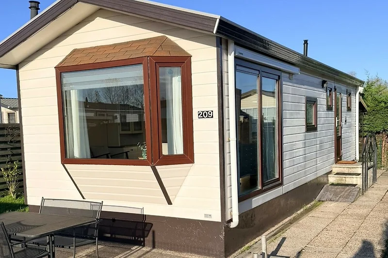 Freistehender Caravan mit großzügigen Fenstern und Außensitzplatz.