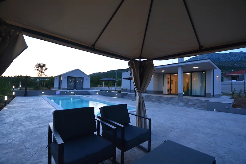 Pergola, Pool und überdachte Sitzgruppe im sonnigen Innenhof.