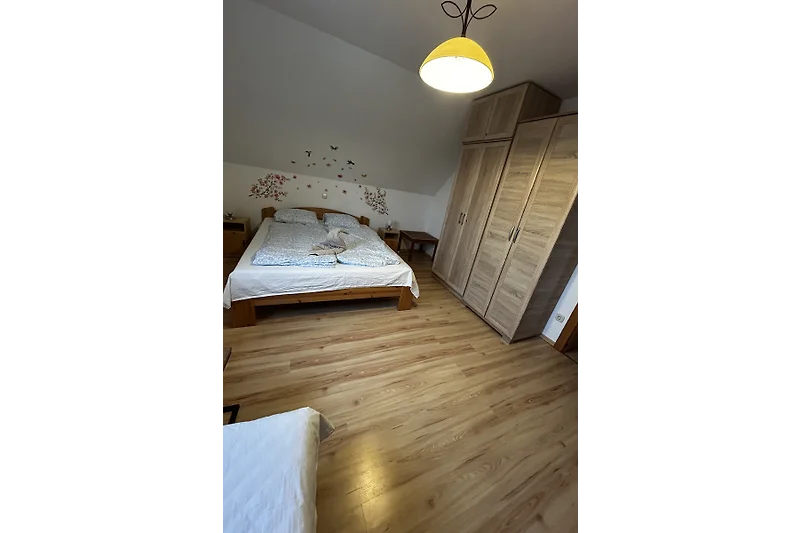 Schlafzimmer mit großem Bett, Nachttisch, Kommode und Vorhängen.
