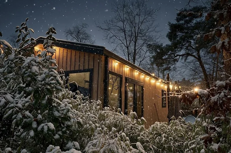 Blockhütte im Schnee, umgeben von verschneiten Tannen bei Nacht.