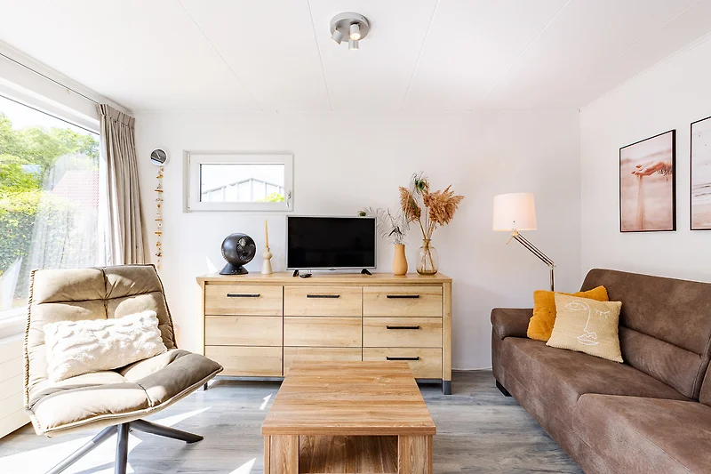 Wohnbereich mit Sofa, Sessel, Esstisch, Pflanzen und TV.