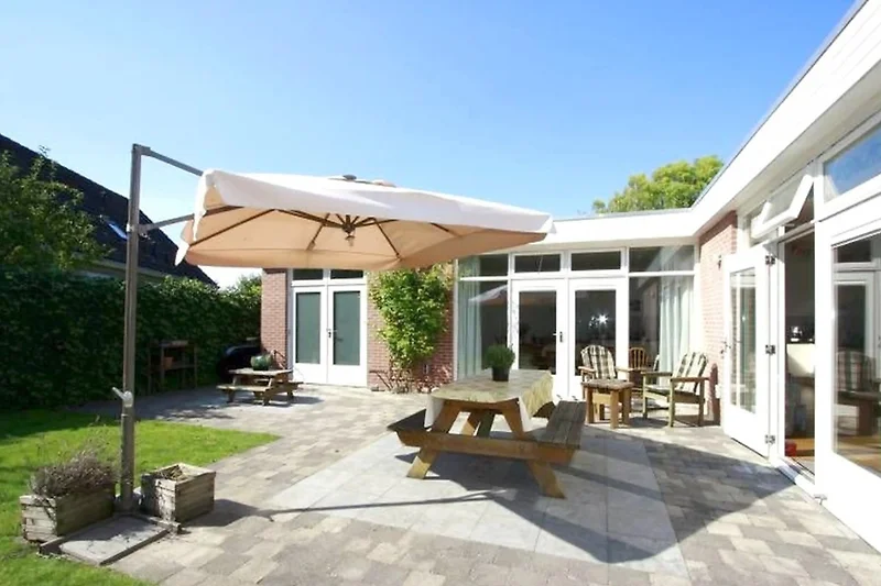 Großer Garten mit Terrasse, Sitzgruppe, Pflanzen und gepflegtem Rasen.