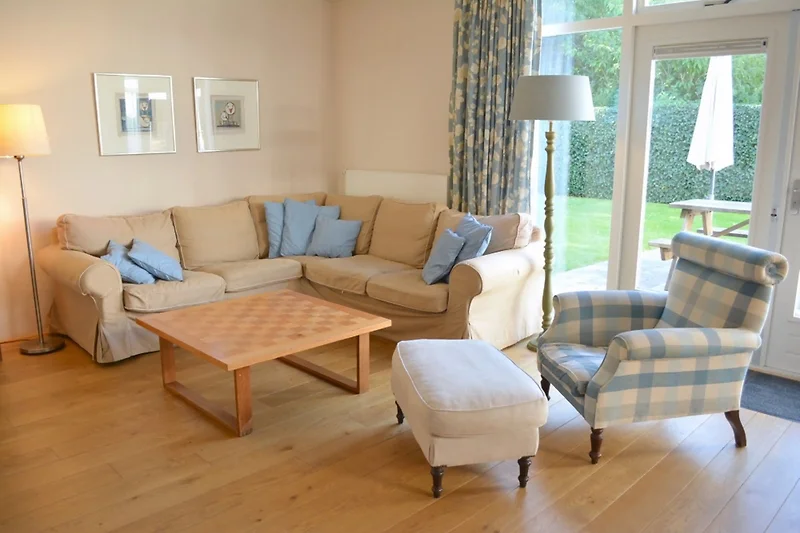 Wohnzimmer mit Sofa, Sessel, Couchtisch, Pflanzen und großem Fenster.