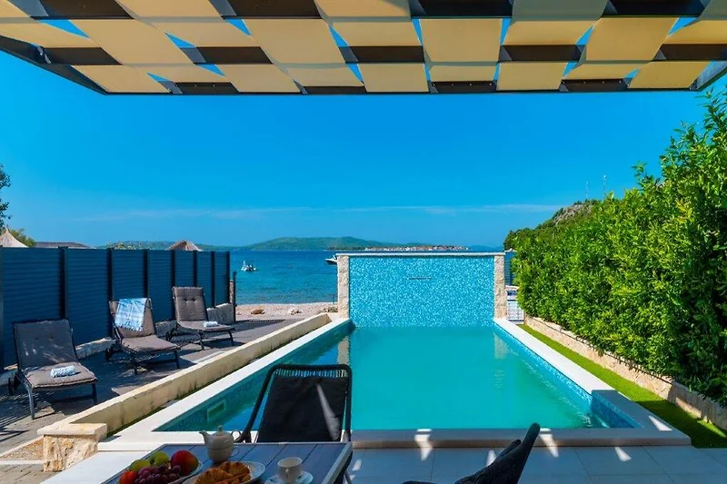 Pool mit Meerblick, Sonnenliegen, Schirmen und tropischem Flair.