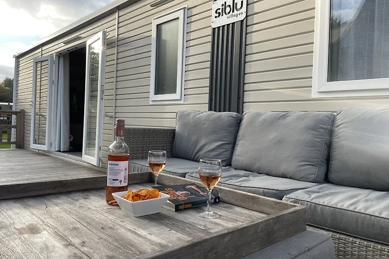 Mobile Home mit Holzterrasse und bequemer Sitzgruppe im Freien.