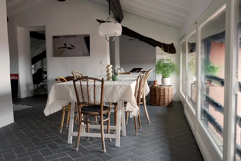 Essbereich mit Holztisch, grauen Stühlen, Pflanzen und Lampen.