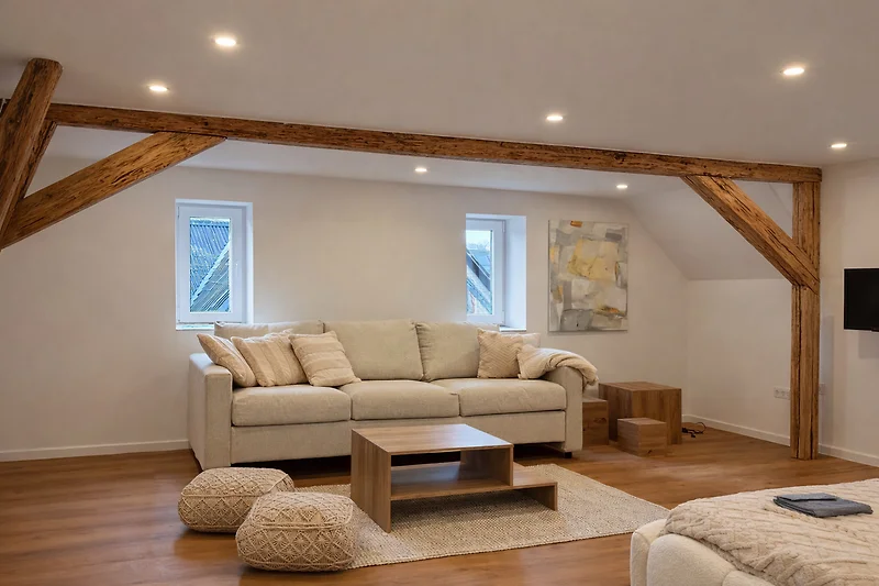 Offener Wohnbereich mit Holzbalken, Sofa, Sessel und Tageslicht.