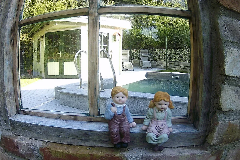 Kind am Fenster mit Glas, Tageslicht und Blick in den grünen Garten.