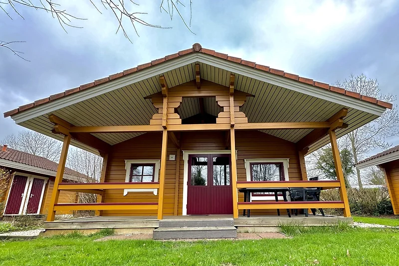 Blockhütte mit Veranda, Holzfassade, Satteldach und Gartenbereich.