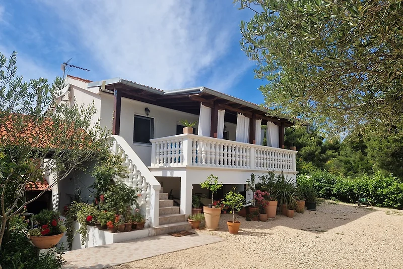 Grüner Garten mit Blumen, Veranda, Treppe und traditionellem Haus.
