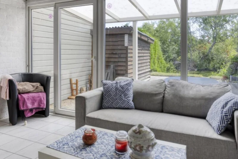 Großes Sofa mit Kissen, Tagesbett, Couchtisch und Pflanzen am Fenster.