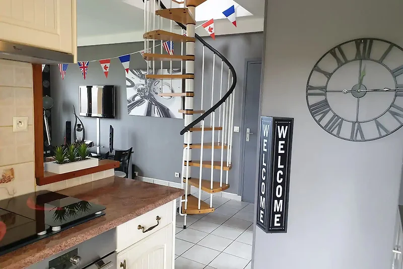 Offene Loft-Etage mit Holztreppe, Regalen, Pflanzen und Designerleuchte.