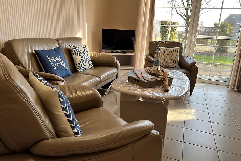 Leder-Sofa, Sessel und Couchtisch vor großen Fenstern mit Vorhängen.