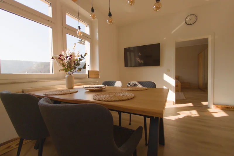 Esszimmer mit großem Holztisch, Glasleuchten und grüner Zimmerpflanze.