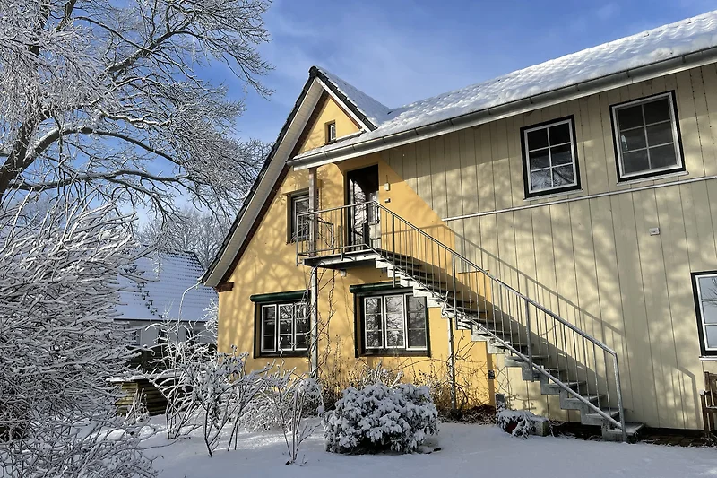 Historisches Haus im Schnee mit Sprossenfenstern und verschneitem Dach.
